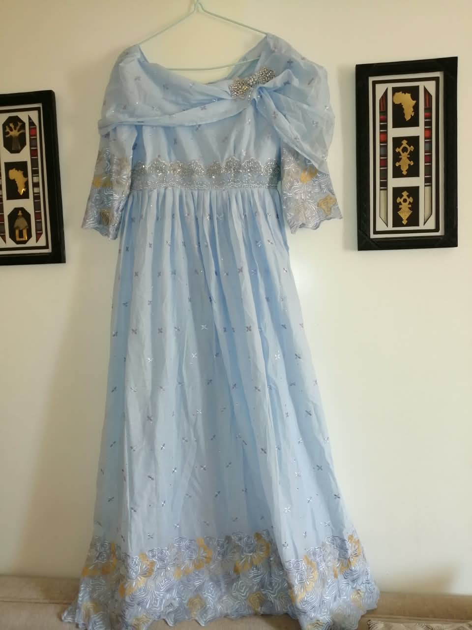 Robe longue bleu ciel avec drapé d'épaule, broche strass et broderies dorées en bas de jupe, création MANDINGK